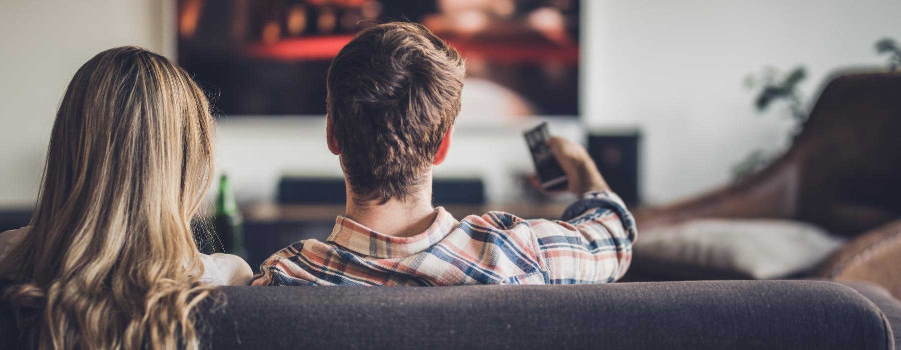 Man and woman sitting on a couch watching a television