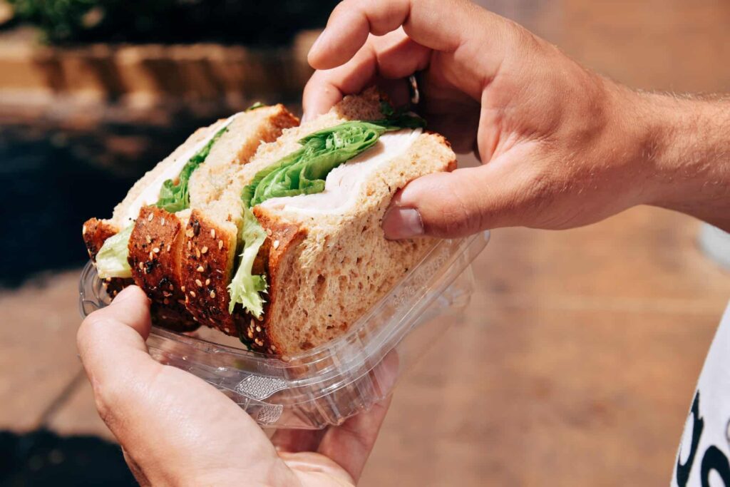 Hands holding a deli sandwich in a takeout container